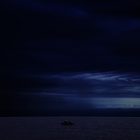 A small boat on a dark, calm ocean at night.