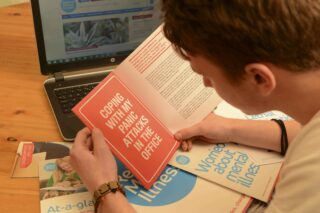 Man reading leaflet that says 'coping with my panic attacks in the office'