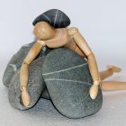 prone wooden figure lying on stones with a stone on its back