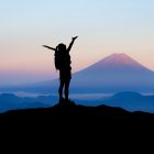 silhouette of a woman stood on top of a mountain with arms outstretched